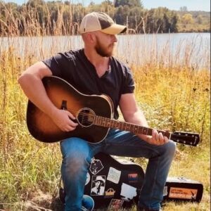 photo of Scott Bogard holding a guitar outdoors near a lake
