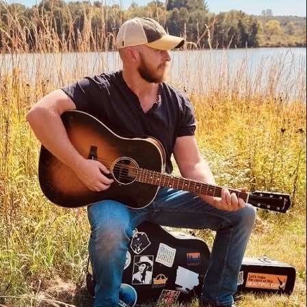 photo of Scott Bogard holding a guitar outdoors near a lake